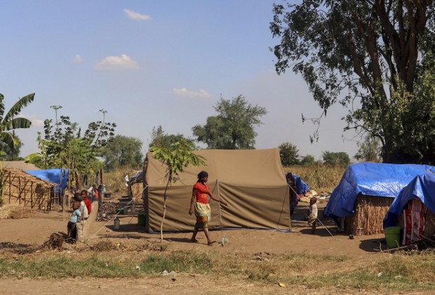 People standing outside of make shift shelters.  Over 25,000 internally displaced people are stranded in Metuge, a town in Cabo Delgado Province, northern Mozambique.